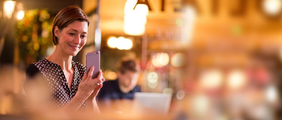 A lady sat at a desk looking at her mobile phone and smiling