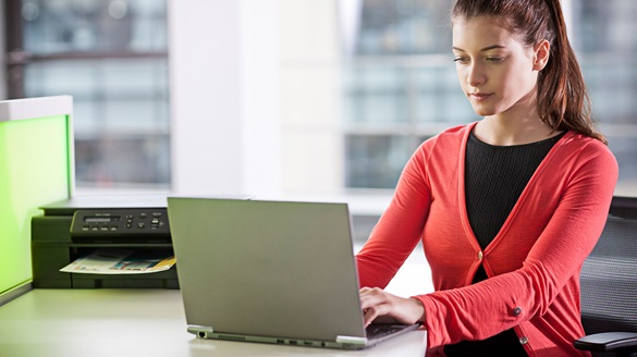 Business man in an office working on his laptop with a Brother printer in the background